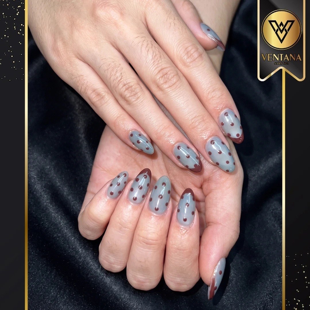 Sheer grey almond nails with a dark polka dot pattern
